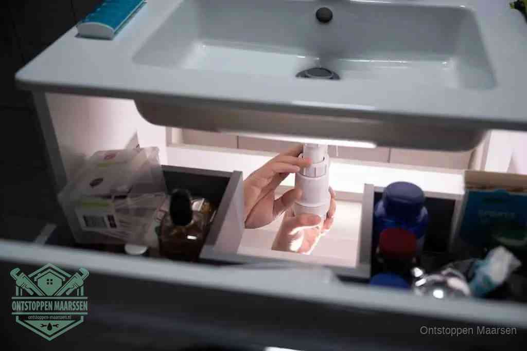 Een pompfles met zeep boven een wastafel, de heet water en afwasmiddel-methode om een vetprop in de afvoer los te maken in Maarssen