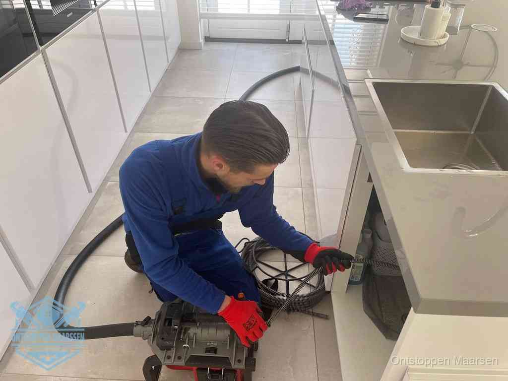 Een monteur ontstopt de keukenafvoer onder de spoelbak met een elektrische veermachine in Maarssen