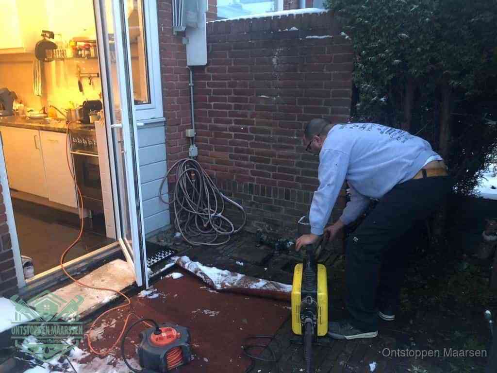 Een monteur werkt buiten bij een open riool-/grondput met een elektrische ontstoppingsmachine om een verborgen afvoerprobleem op te sporen in Maarssen