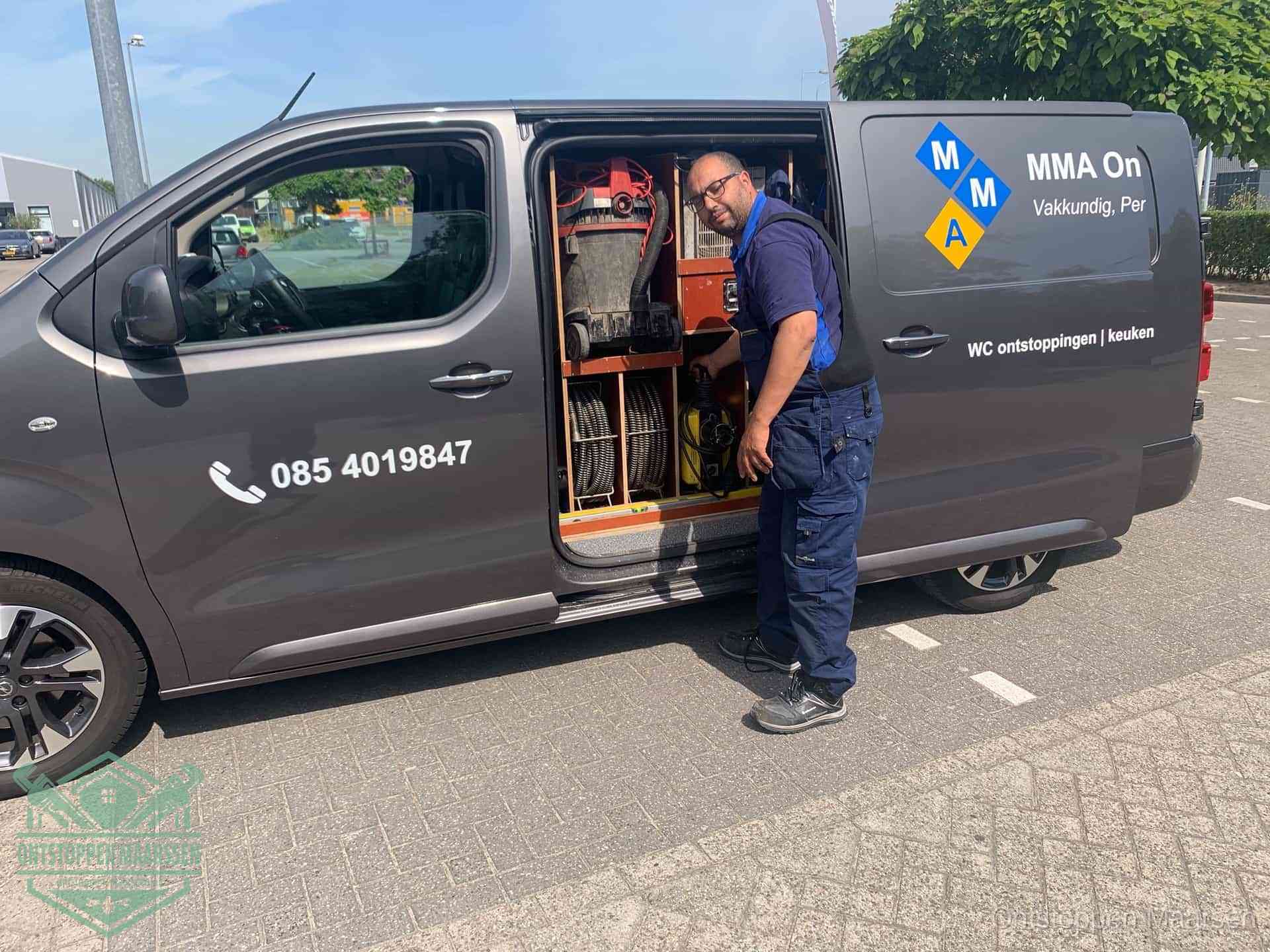 Een monteur bij de open schuifdeur van zijn bedrijfsbus op een parkeerplaats, klaar om de oorzaak van terugkerende afvoerverstoppingen aan te pakken in Maarssen
