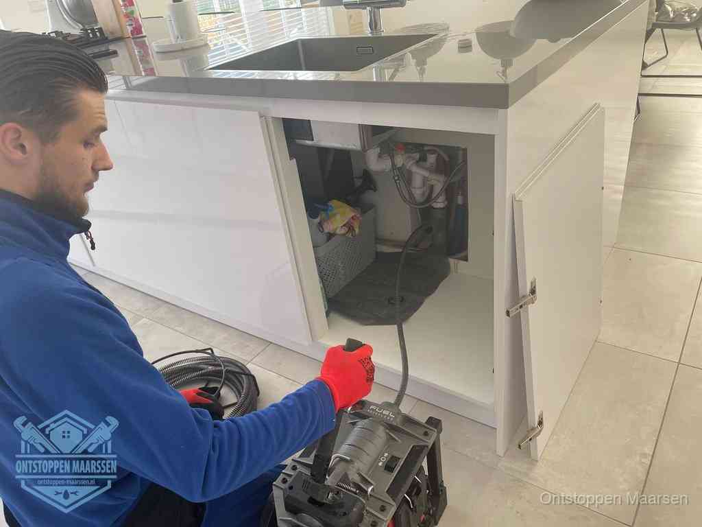 Monteur ontstopt met een veermachine een verstopte afvoer onder de gootsteen in Maarssen
