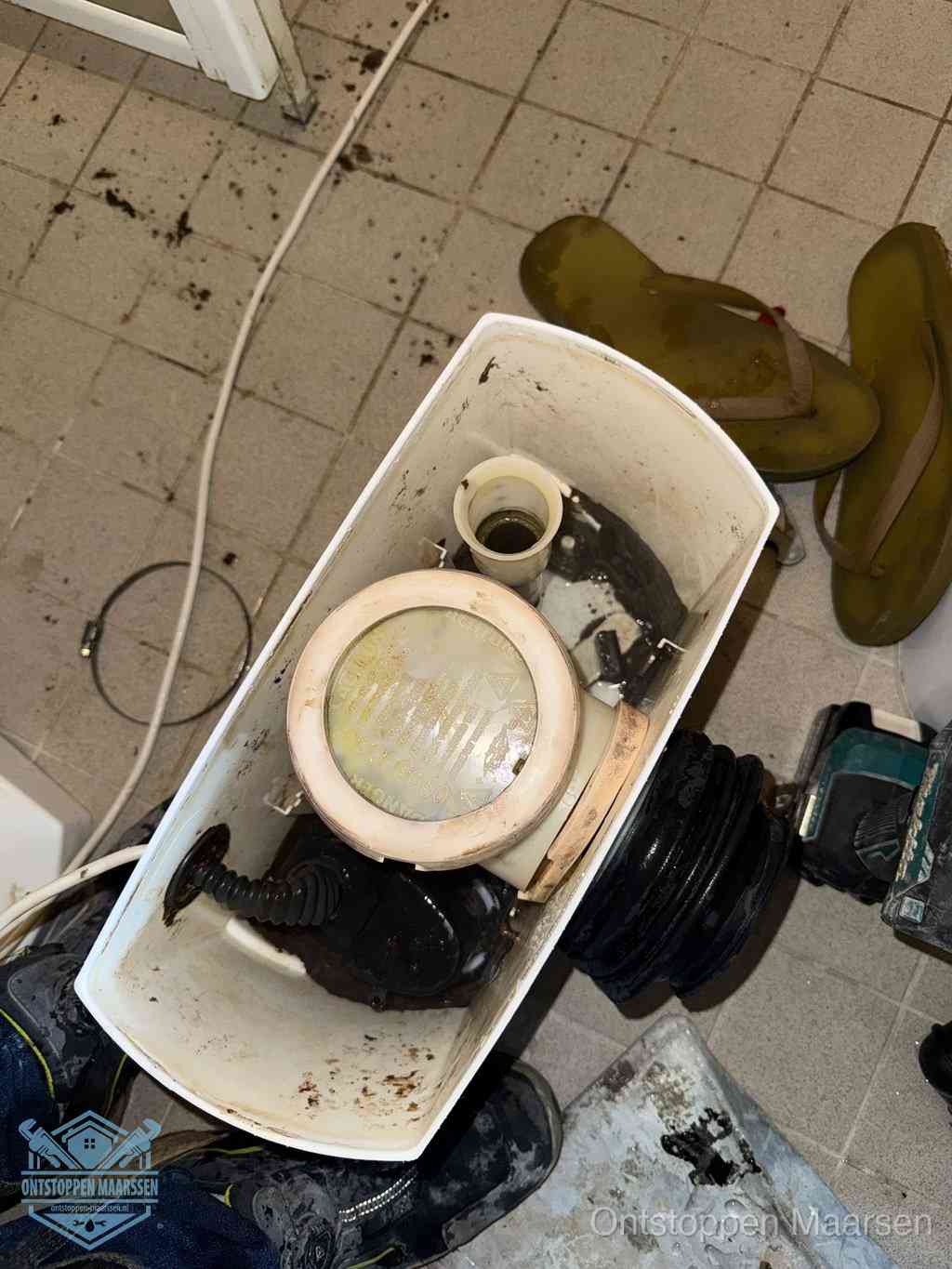 Een gedemonteerde toiletpot op de vloer met ontstoppingsveer en gereedschap ernaast, het verwijderen van een vastzittend voorwerp uit de wc in Maarssen