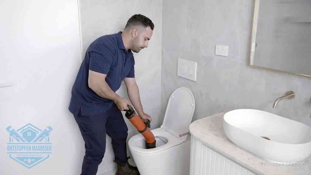 Een man gebruikt een handmatige luchtdruk-ontstopper in een modern betegeld toilet om zelf de wc te ontstoppen in Maarssen